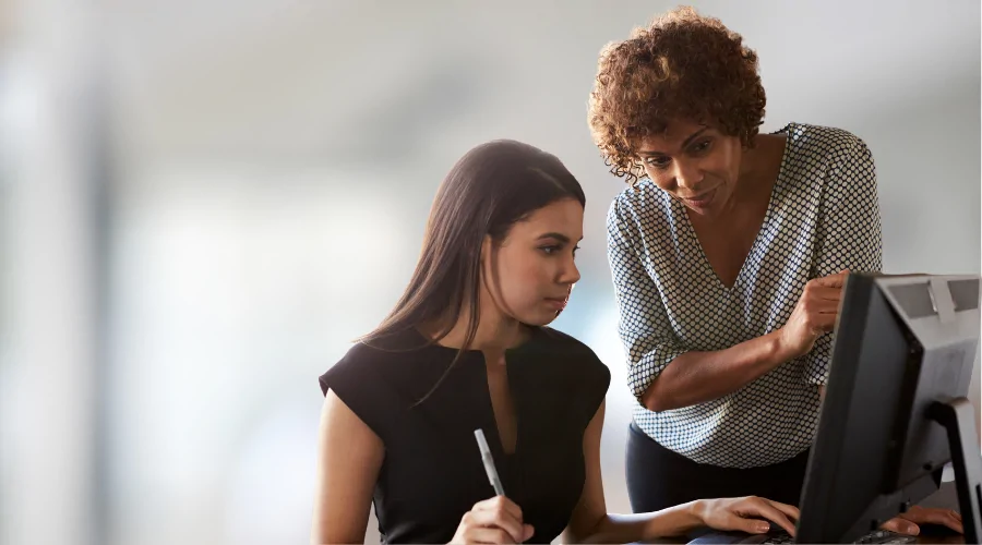 Manager training an employee who is using a computer