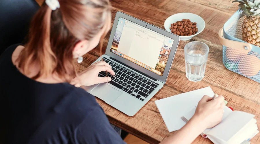 A person writing notes whilst using a laptop
