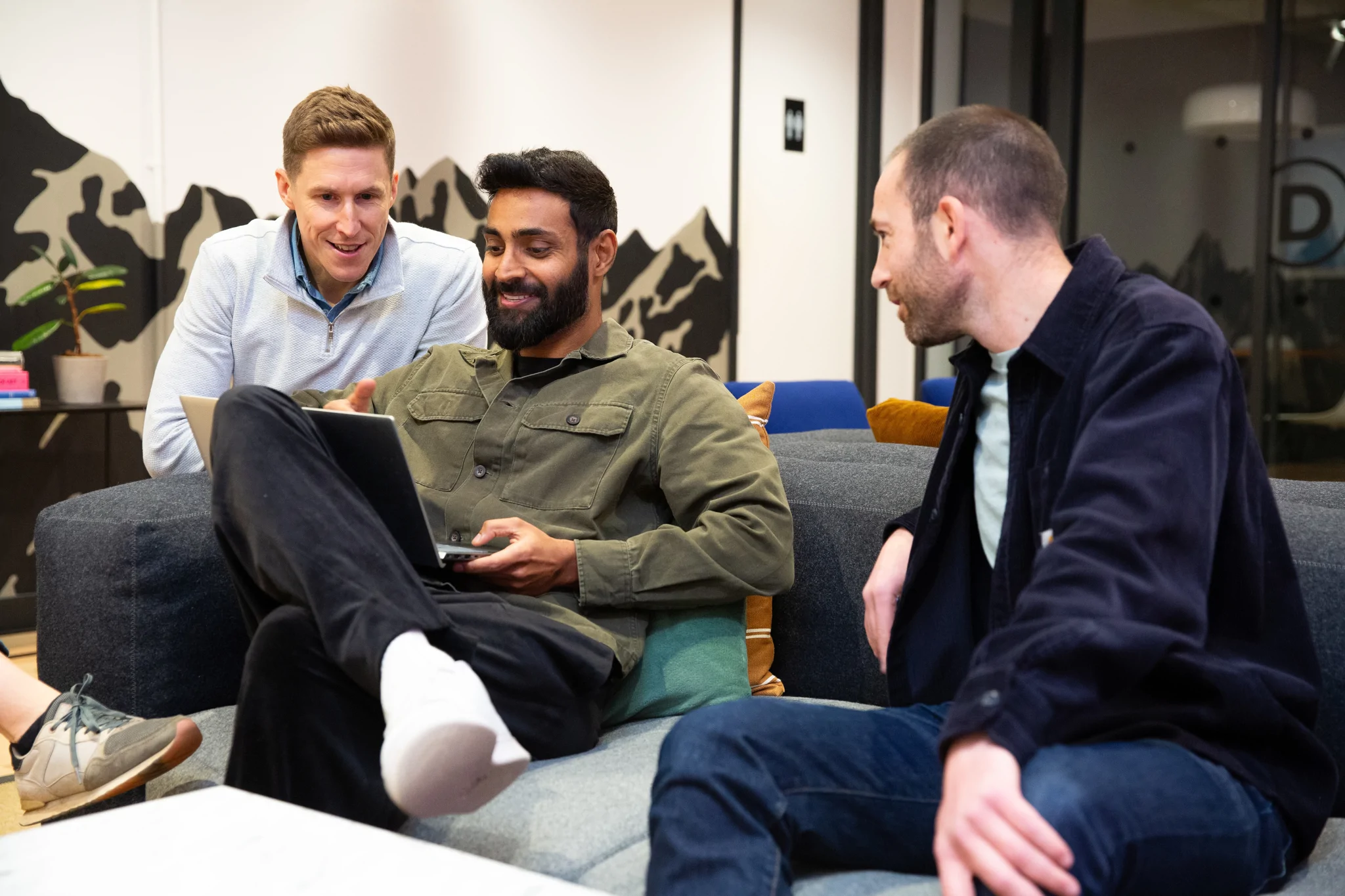 three men look at a laptop