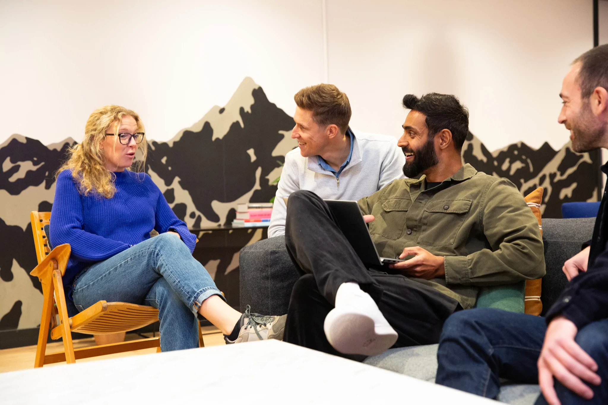 Four people sat around talking one holding a laptop