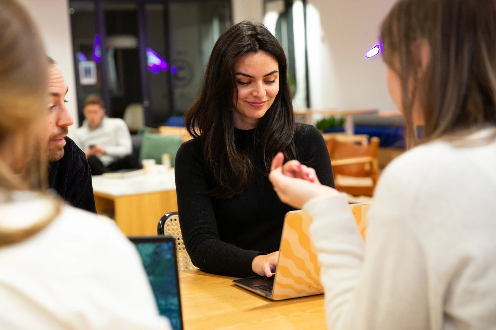 Girl typing on her laptop sitting across from colleagues