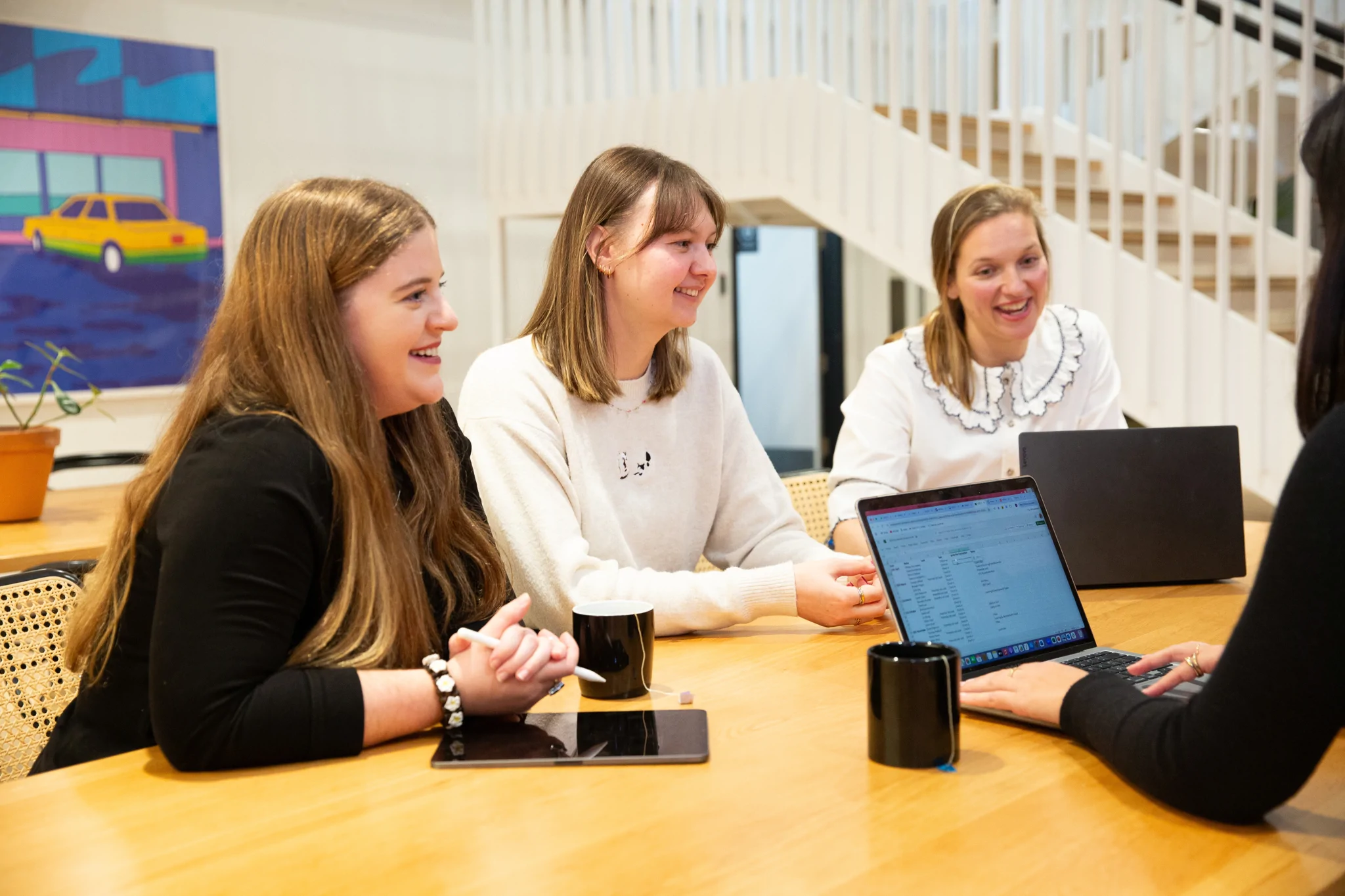 Three women sat at a table looking at another person